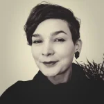 Profilbild von Kristin Lübken. Sie lächelt in die Kamera und trägt dunkle Kleidung.